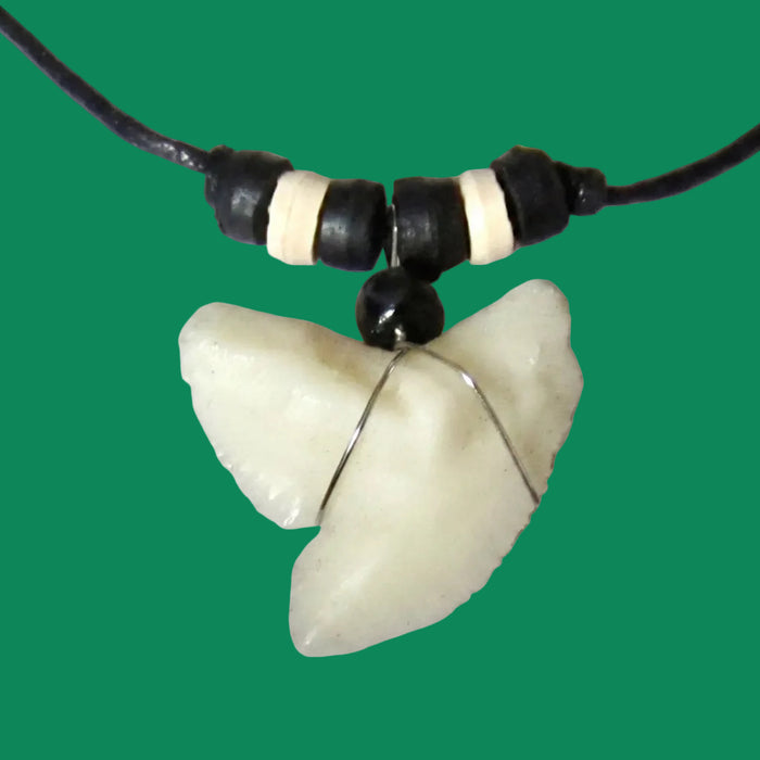 A pendant necklace with a black cord, black and cream beads, and a silver wire wrap, shown against a solid green background.